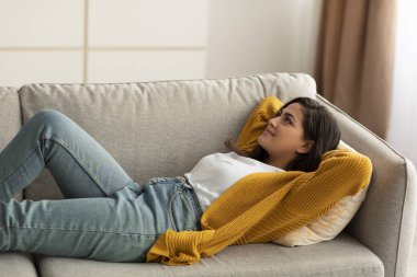 Haftasonu rahatlama. Sakin Arap kadın kanepede dinleniyor ve hayal kuruyor, kanepede uzanmış, elleri başının arkasında, boş yer var.