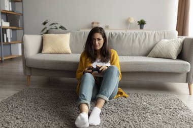 Oyun çubuğuyla oyun oynayan, halının üzerinde oturup bilgisayar oyunlarıyla eğlenen ciddi bir Arap kadın.