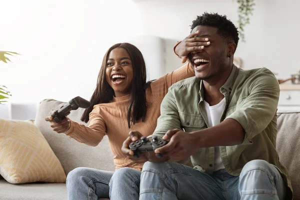 Laughing black woman closing boyfriend eyes, playing video games — Stock Fotó