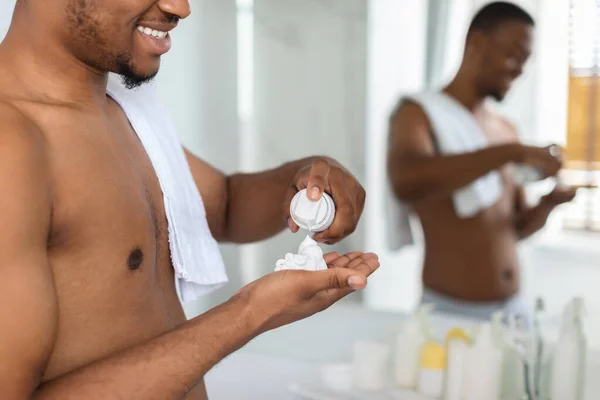 Hombre negro aplicando espuma de afeitado en el brazo en el baño, preparándose para el afeitado — Foto de Stock