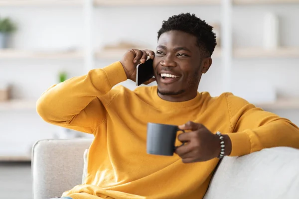 Cheerful black guy having phone conversation with friend, drinking tea — Stockfoto