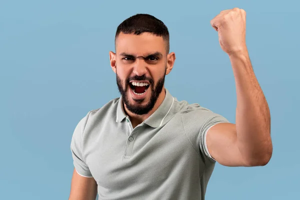 Angry middle eastern guy shaking clenched fist at camera and shouting, showing his protest over blue background — Zdjęcie stockowe