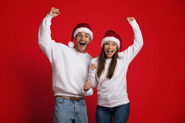 Overjoyed Couple In Santa Hats Emotionally Celebrating Success With Raised Fists — стокове фото
