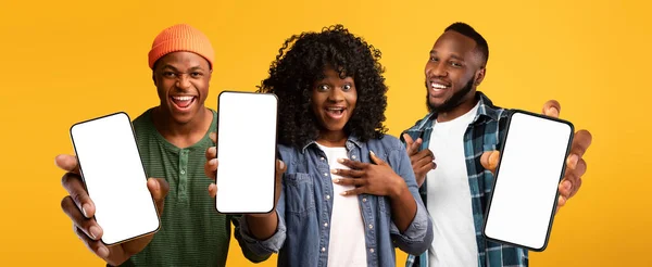 Три захоплені чорні люди, які показують смартфони з білим порожнім екраном, макет — стокове фото