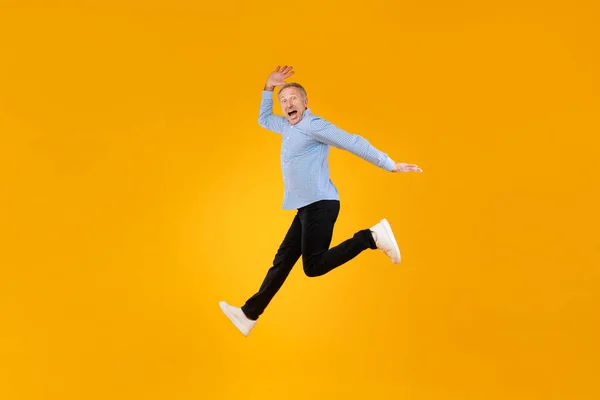 Excited mature man jumping up at orange studio — Stockfoto
