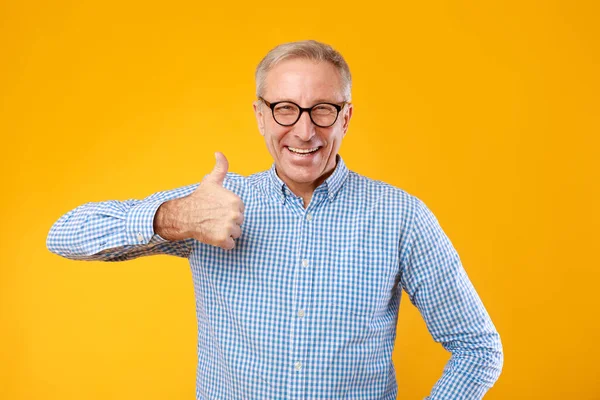 Happy mature man gesturing thumbs up and smiling at studio —  Fotos de Stock