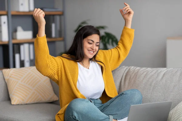 Overjoyed arab lady sitting on sofa with laptop, gesturing YES, celebrating success at home, free space — Stockfoto