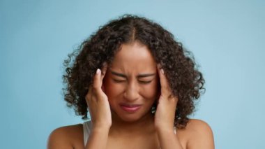 African Woman Suffering From Headache Massaging Temples Over Blue Background