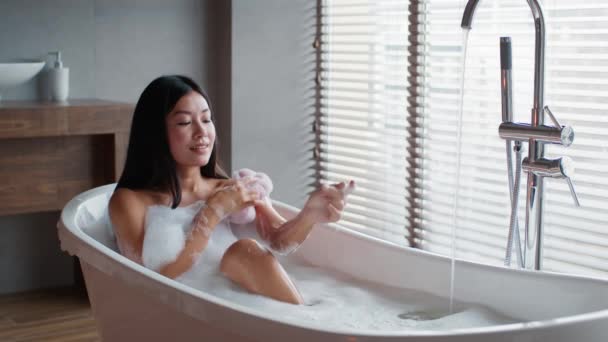 Asian Lady Taking Bath Rubbing Arm With Sponge In Bathroom — Vídeo de Stock