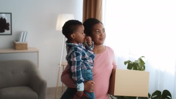 Relocation Concept. Black woman with son on hands walking in new flat — Stockvideo