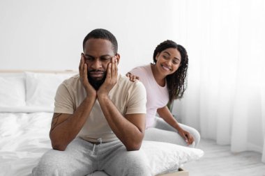 Gülümseyen genç siyah eş üzgün kocaya sakinlik, yatak odasında iç tarafta oturmak.