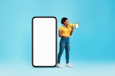 Mutlu siyah kadın megafona bağırıyor, dev akıllı telefonun yanında boş ekranla duruyor, tasarım için maket yapıyor.