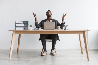 Masada dizüstü bilgisayarla beyaz duvara yaslanmış afro-amerikan genç iş adamının tam boy portresi.