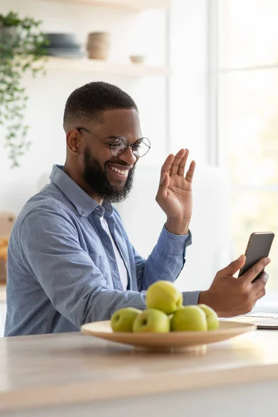 Happy young handsome african american businessman with beard in glasses waving hand at smartphone — Stock Fotó