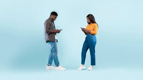 คู่รักชาวแอฟริกันอเมริกันใช้โทรศัพท์มือถือ กําแพงสตูดิโอสีฟ้า — ภาพถ่ายสต็อก