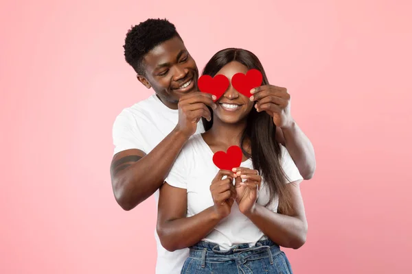 Unga romantiska svarta par täcker ögon med röda papper hjärtan — Stockfoto