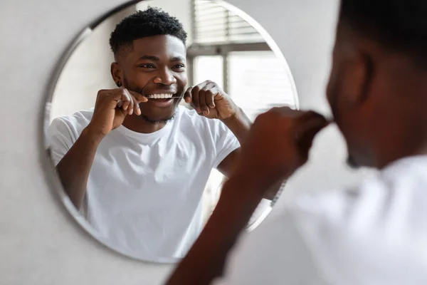 Black guy flossing teeth with tooth floss near mirror indoor — Fotografie, imagine de stoc