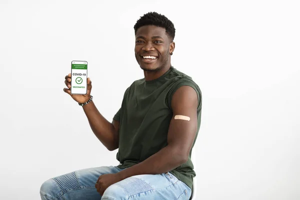 Cheerful vaccinated black guy showing smartphone with certificate — 스톡 사진