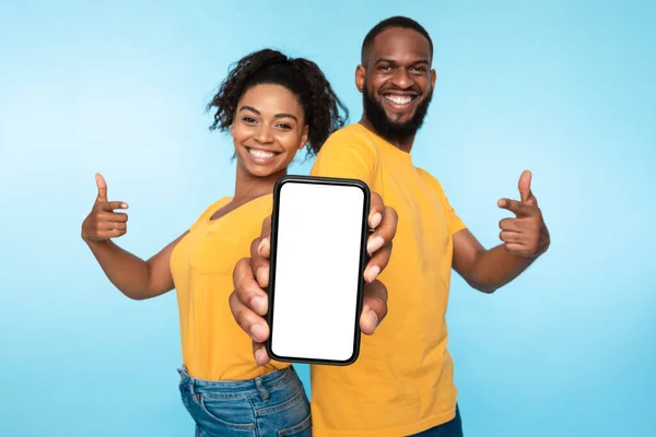 Utilice esta nueva aplicación genial. Positiva pareja afroamericana apuntando al teléfono inteligente con pantalla blanca en blanco, maqueta —  Fotos de Stock