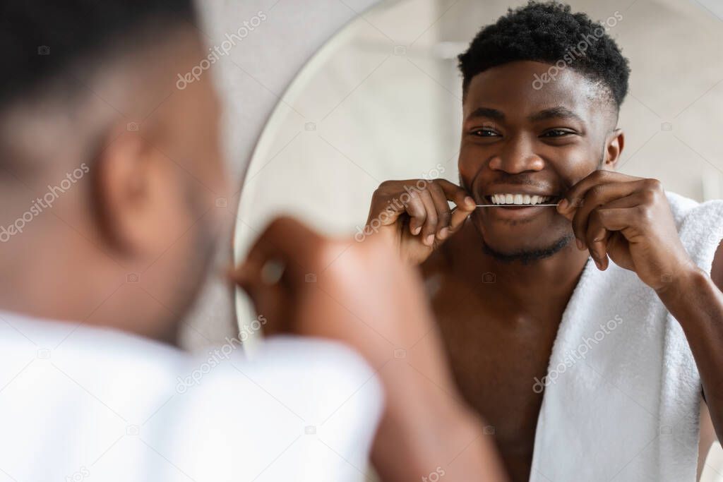 Cheerful black man using teeth floss in bathroom