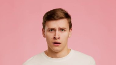 Anxious Young Man Expressing Fear Raising Eyebrows Over Pink Background