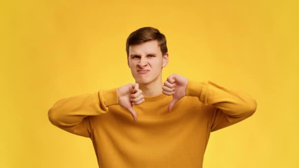 Δυσαρεστημένος άνθρωπος gesturing αντίχειρες κάτω με τα δύο χέρια, κίτρινο φόντο — Αρχείο Βίντεο