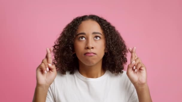 Чорна жінка тримає пальці схрещеними для удачі, рожевий фон — стокове відео