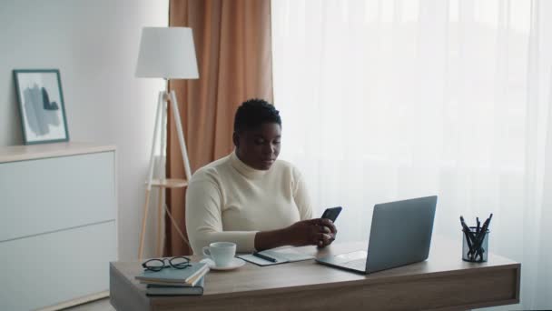 African Businesswoman Using Smartphone Texting Looking At Laptop In Office — Stockvideo