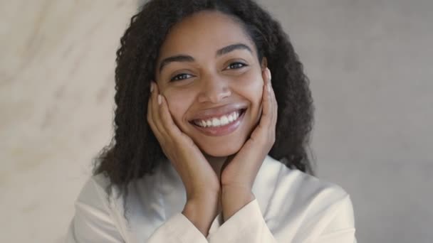 Natural beauty concept. Close up of young positive african american lady smiling at camera, touching her smooth cheeks — ストック動画