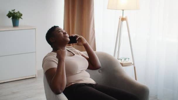 Щаслива чорна леді розмовляє по телефону сміється сидячи вдома — стокове відео