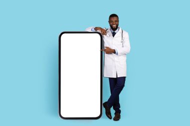 Üniformalı, gülümseyen siyah doktor beyaz perdeli, boş telefona işaret ediyor.