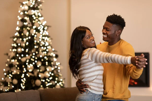 Noel ağacının yanında dans eden neşeli siyah çift içeride tatili kutluyor.