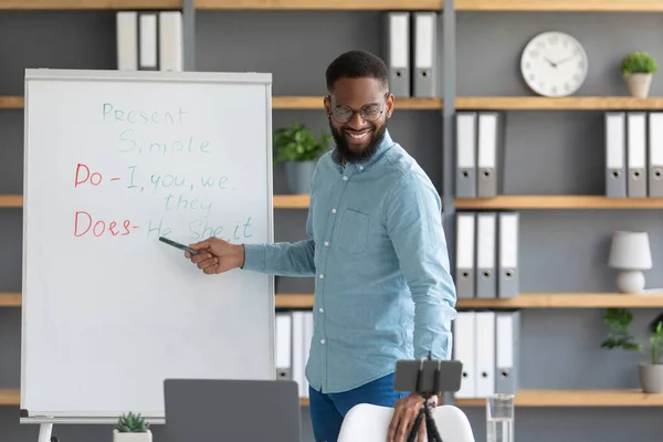 Glad friendly millennial african american male blogger teacher points to English rules on blackboard —  Fotos de Stock