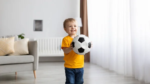 Favoritspel. Glad småbarn man unge håller fotboll i händerna och ler när du spelar hemma, panorama — Stockfoto