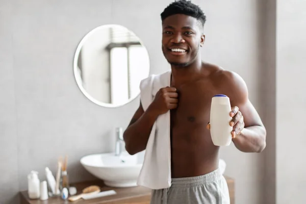 Africano chico mostrando shampo botella publicidad macho cosmético en cuarto de baño — Foto de Stock