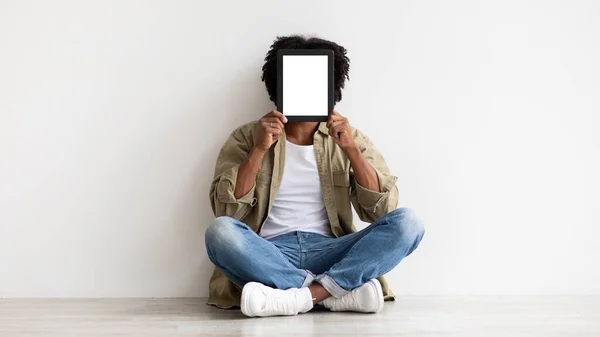 Black Man Covering Face With Blank Digital Tablet While Sitting On Floor — Fotografia de Stock