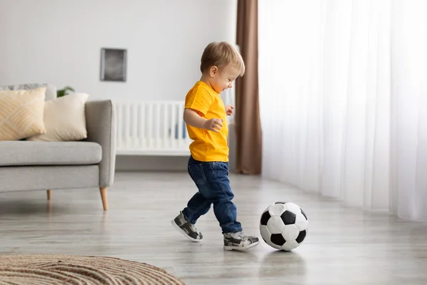 Future champion. Adorable little toddler boy playing football, hitting ball at home, having fun in living room — ストック写真
