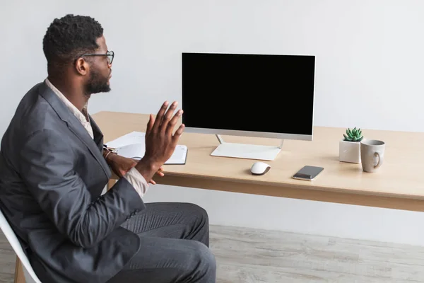 Молодий чорний підприємець, що проводить онлайн бізнес-зустріч в офісі, махає на моніторі комп'ютера з порожнім екраном, макет — стокове фото