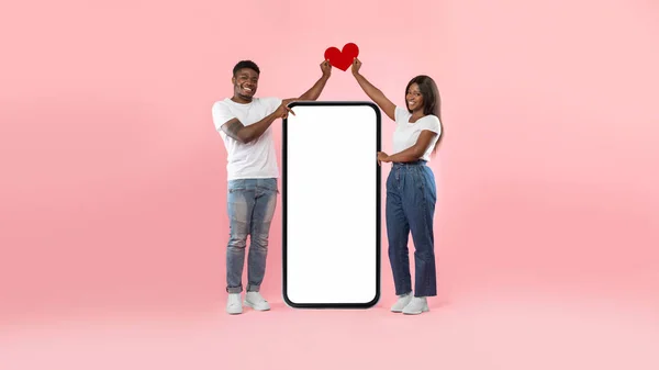 Couple showing white empty smartphone screen holding paper heart — Stockfoto