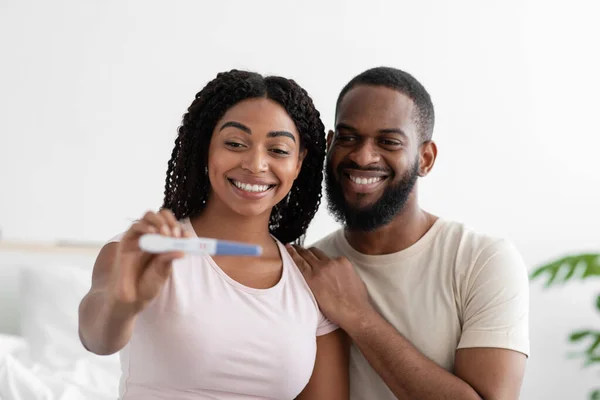 Spokojeni atraktivní tisíciletý černošky žena a chlap show pozitivní těhotenský test na kameře v ložnici interiér — Stock fotografie