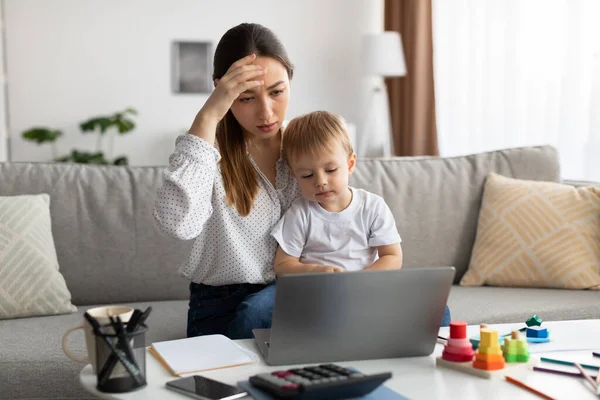 Tekanan kerja jarak jauh. Ibu yang lelah menggendong anak balita dan melihat laptop, mengalami masalah dengan pekerjaan jarak jauh — Stok Foto