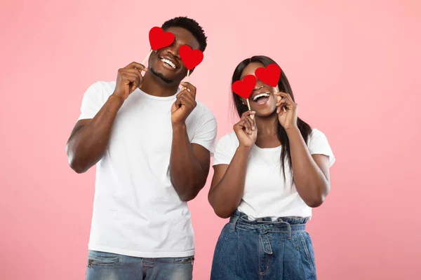Unga romantiska svarta par täcker ögon med röda papper hjärtan — Stockfoto