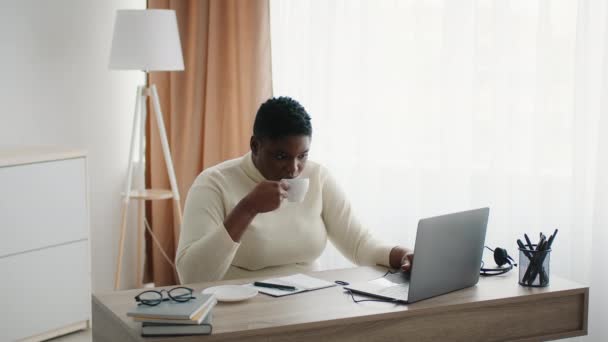 Plus-Sized Black Woman Working On Laptop Drinking Coffee In Office — Stockvideo