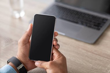 Tanımlanamayan bin yıllık Afro-Amerikan iş adamı iş yerinde boş ekranlı akıllı telefon tutuyor.