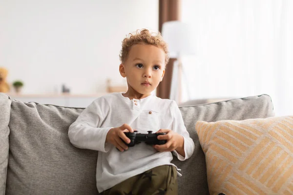 Africano pequeño niño jugando videojuegos celebración controlador en casa — Foto de Stock