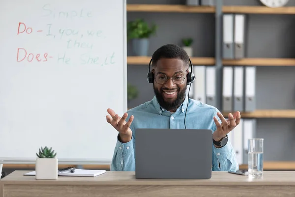 Ευτυχής νεαρός Αφρικανός Αμερικανός δάσκαλος ή δάσκαλος χειρονομίες με τα χέρια και κοιτάζει οθόνη υπολογιστή στο σπίτι — Φωτογραφία Αρχείου