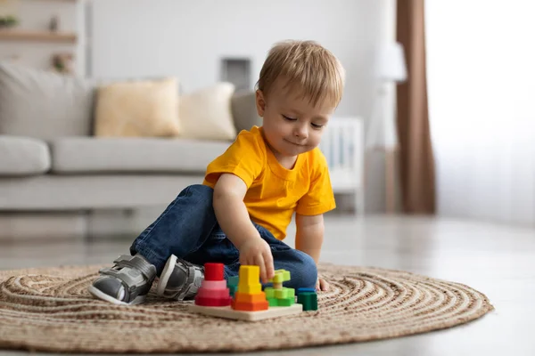 Adorable little boy playing with educational wooden toy at home, sitting on floor carpet in living room, copy space — Fotografia de Stock