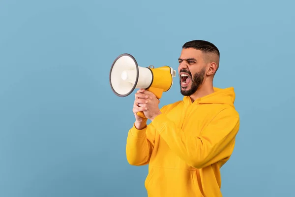 Emocional hombre de Oriente Medio gritando con megáfono, haciendo anuncio o compartiendo noticias, fondo azul — Foto de Stock