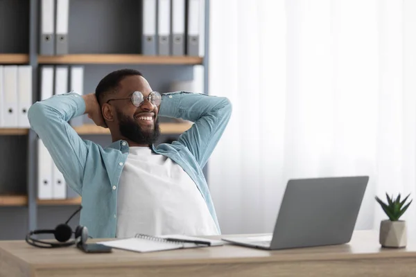 Sonriendo relajado millennial afroamericano masculino con barba en gafas con las manos detrás de la cabeza disfrutando del descanso — Foto de Stock