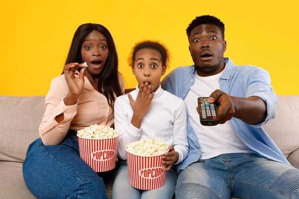 Surprised young family watching television with popcorn sitting on sofa — Stockfoto